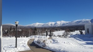 A snow-covered pathway leading to a building with a view of snow-capped mountains. - Bretton Woods White Mtn Getaway-fall foliage, mountain views & skiing await (Bretton Woods)