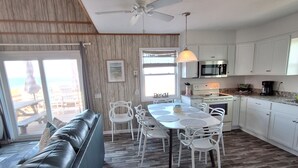 A modern kitchen with white cabinets, a dining table with white chairs, and a ceiling fan. - Right on the Beach and Dog Friendly! (Kitty Hawk)