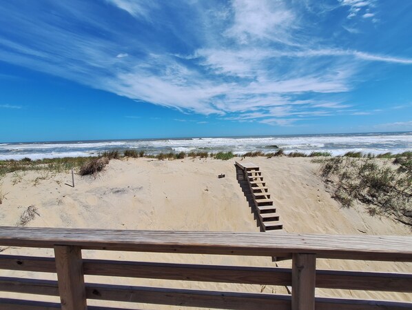 A wooden deck leading to a sandy beach with ocean waves in the background.