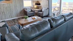 A modern living room with a leather sofa, two armchairs, a coffee table, and a TV mounted on the wall. - Right on the Beach and Dog Friendly! (Kitty Hawk)