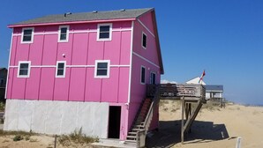A pink lifeguard tower with a wooden staircase leading up to it, situated on a sandy beach with a clear blue sky. - Right on the Beach and Dog Friendly! (Kitty Hawk)