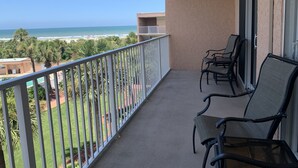 Ein Balkon mit Blick auf Strand und Meer. Zwei Stühle und ein Tisch befinden sich auf dem Balkon.