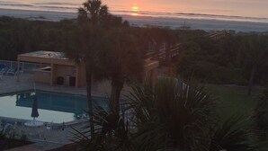 Ein Sonnenuntergang über einem Strand mit Pool und einem kleinen Gebäude.