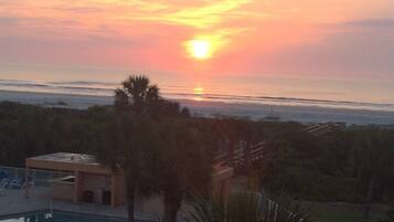 A sunset over a beach with a pool and a small building.