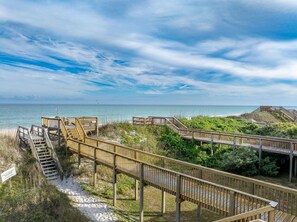 A wooden boardwalk leading to a beach with a clear view of the ocean.