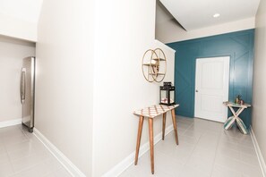 Un couloir avec un réfrigérateur, une table recouverte d’une nappe à motifs et une porte agrémentée d’un mur d’accent de couleur turquoise.