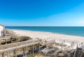 A beach view with wooden boardwalks leading to the shore, a clear sky, and a calm sea. - Toes in the Water - Luxury Oceanfront 5 BR 5.5 Bath; Hot Tub; Elevator (North Topsail Beach)