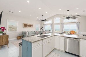 A modern kitchen with a central island, a dishwasher, and a ceiling fan. - Toes in the Water - Luxury Oceanfront 5 BR 5.5 Bath; Hot Tub; Elevator (North Topsail Beach)