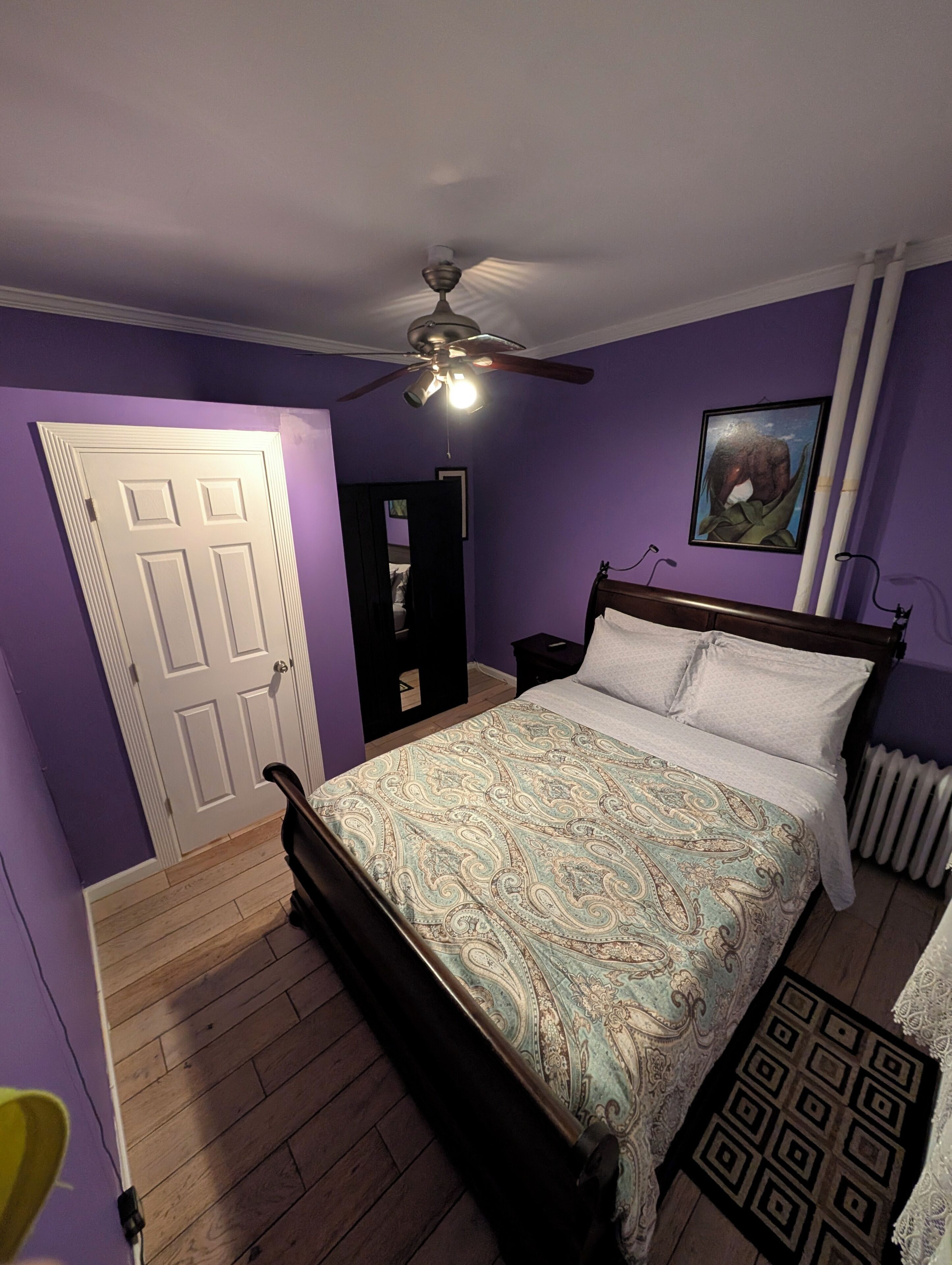 Een slaapkamer met een bed, een plafondventilator, een radiator en een deur.