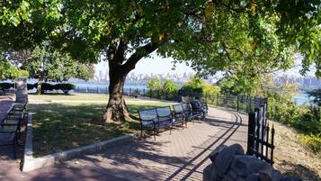 Ein Park mit Bänken, einer Steinsäule und Blick auf eine Stadtlandschaft über dem Wasser.