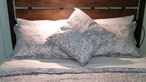 A bed with a wooden headboard, patterned bedding, and a wall-mounted light fixture.