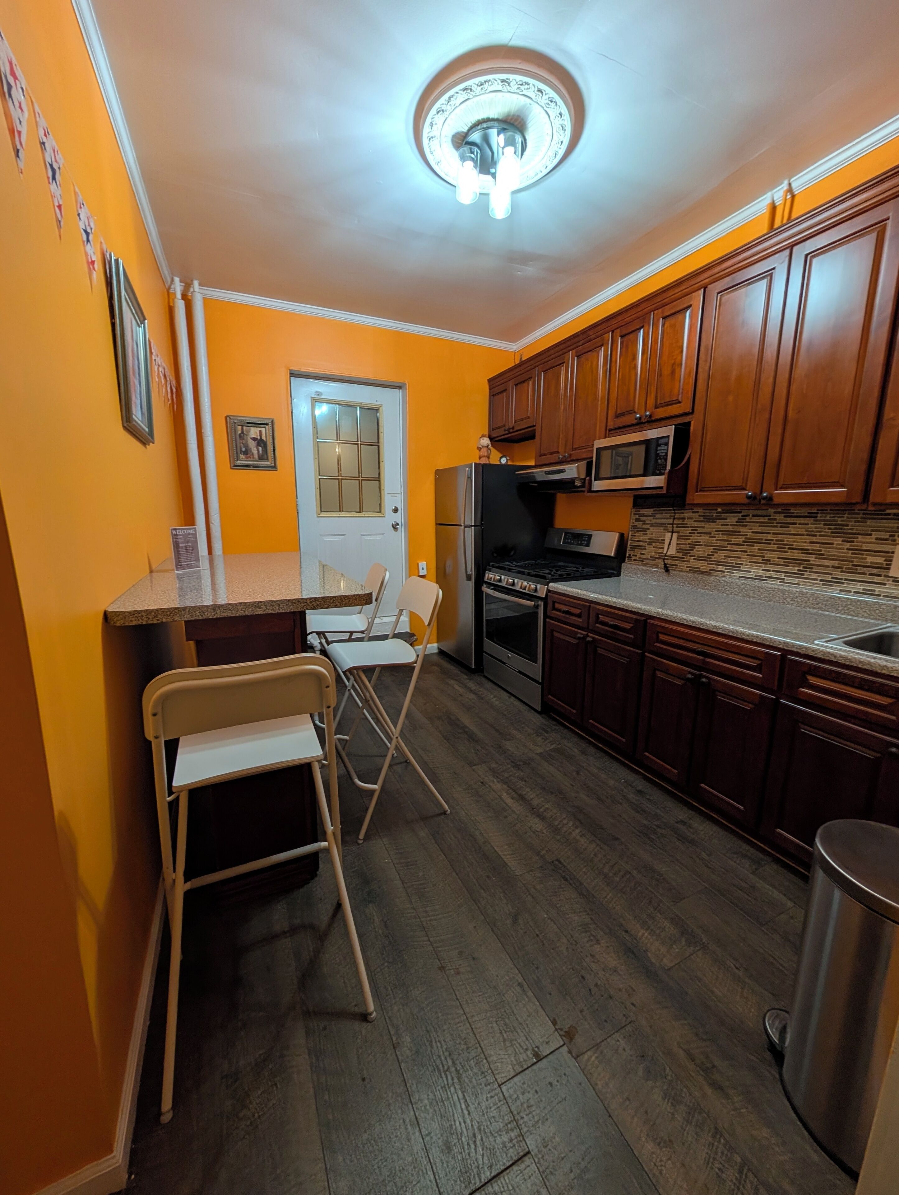 A compact kitchen with wooden cabinets, a stainless steel refrigerator, and a microwave. There is a small dining area with two chairs and a table.