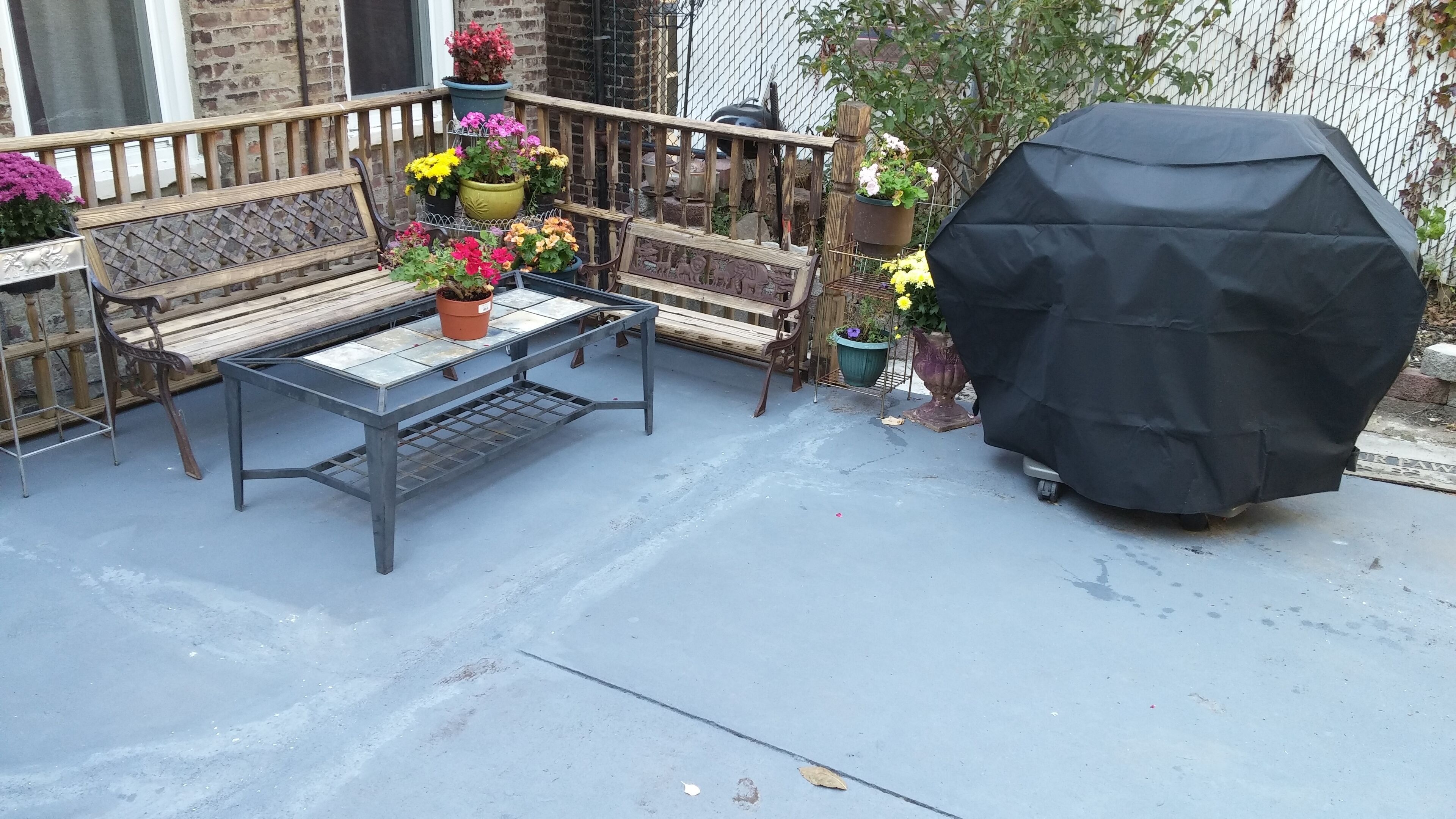 A patio with a metal table, two wooden benches, and various potted plants.