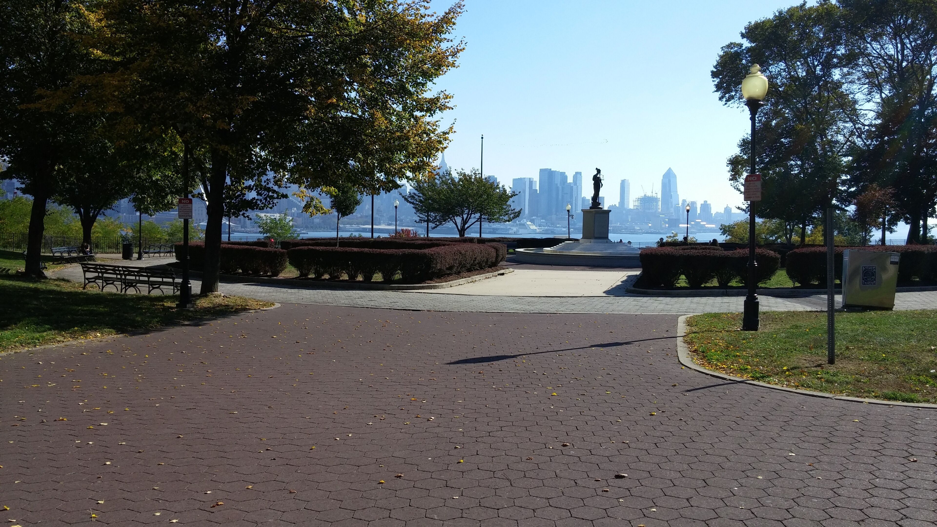 Ein Park mit einem gepflasterten Weg, Bänken und einer Statue.