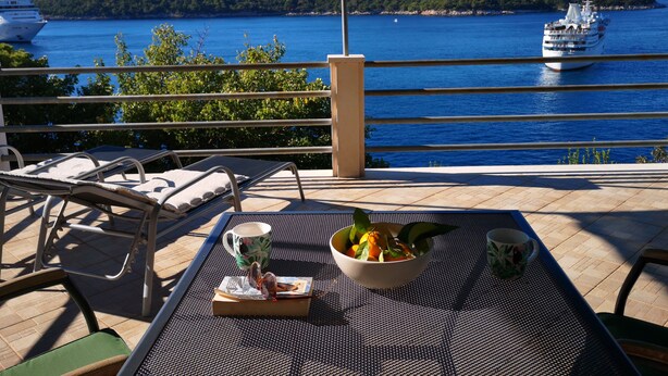 Un balcon avec une table, des chaises et une vue sur la mer, où l’on peut apercevoir des bateaux.