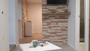 Un salon moderne avec une table basse blanche, des livres et un téléviseur à écran plat fixé au mur, qui est décoré d’un motif imitant la pierre.