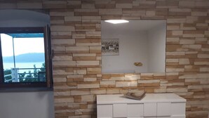 Une pièce avec un mur décoré d’un motif en pierre, un meuble blanc avec des tiroirs et une fenêtre donnant sur un plan d’eau et des collines.
