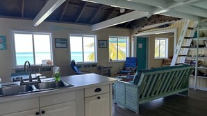 A kitchen with a sink, a chair, and a bench. There are windows with a view of the ocean. - Beachfront large 2/2 on Spanish Wells' northside beach. Sun deck by the water. (Spanish Wells)