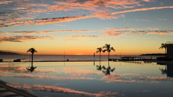 A serene pool area with a sunset view, palm trees, and a clear sky.