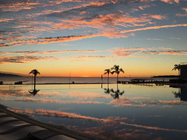 Ein friedlicher Poolbereich mit Sonnenuntergangsblick, Palmen und wolkenlosem Himmel.