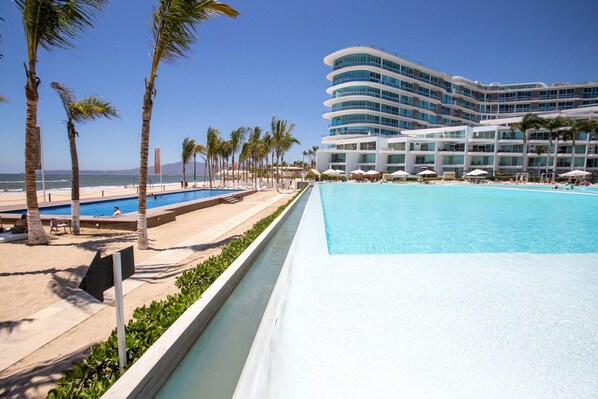 Un hotel con una piscina grande, palmeras y vista al mar.