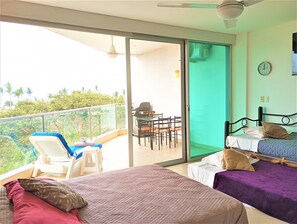 Ein Zimmer mit zwei Betten, einem Balkon mit Tisch und Stühlen sowie Blick auf Grün.