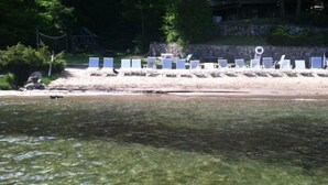 Une plage à l’eau claire, avec un rivage sablonneux et des rangées de chaises longues blanches.