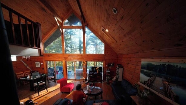 L’intérieur chaleureux d’un chalet comprend un coin repas, un salon avec un canapé, un téléviseur et une grande fenêtre donnant sur une forêt.