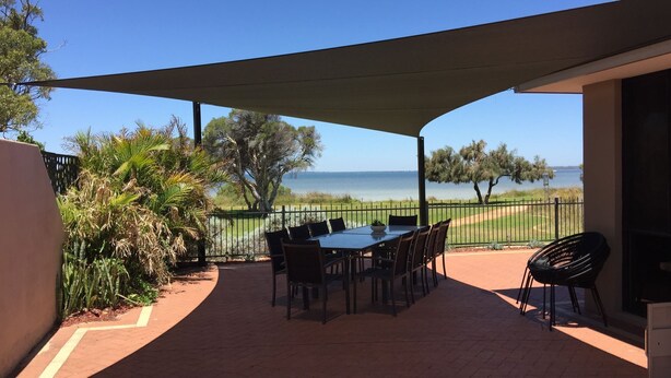 Eine Terrasse im Freien mit Tisch und Stühlen, einem überdachten Bereich und Blick auf das Meer.