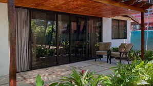 A modern outdoor patio with sliding glass doors, a wooden pergola, and two chairs. - Hotel Tropical Garden (Jacó)