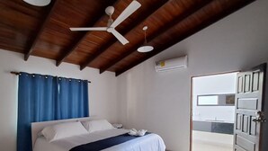 A bedroom with a bed, a bedside table, a ceiling fan, and an air conditioning unit. - Hotel Tropical Garden (Jacó)
