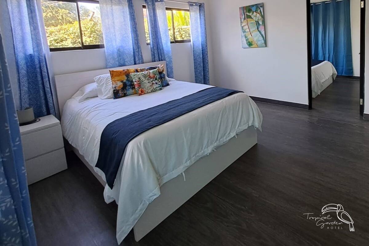 A modern bedroom with a bed, a nightstand, a ceiling fan, and a window with blue curtains.