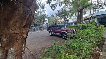Um SUV vermelho estacionado numa entrada com cerca azul e vegetação exuberante.