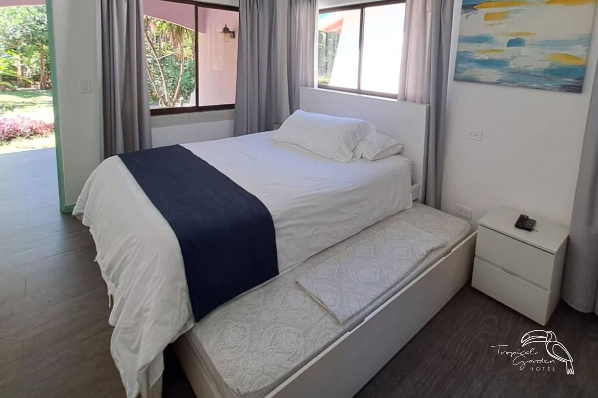 A bedroom with a bed, a bench, a nightstand, and a painting.
