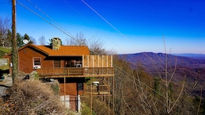 Situated on a hillside, this cabin offers expansive views of the surrounding landscape from its wooden balcony.