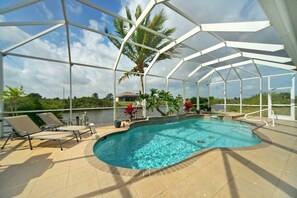 A covered swimming pool with lounge chairs and potted plants, surrounded by a white metal structure. - Gulf Access Canal Home | Heated Pool, Private Dock & Home Office | Pet Friendly | Sleeps 6 (Cape Coral)