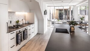 A modern kitchen with white cabinetry, a dark countertop, and a central island. - Collie’s beach house (Mangawhai Heads)