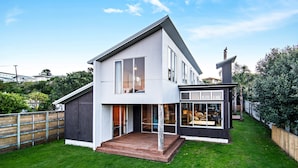 A modern two-story house with a large deck and a covered outdoor seating area. - Collie’s beach house (Mangawhai Heads)