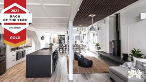 A modern kitchen with a central island, a dining area with a large table, and a cozy seating area with a sofa and bean bag. - Collie’s beach house (Mangawhai Heads)