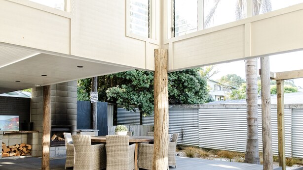 An outdoor patio area with wicker furniture, a wooden table, and a potted plant. - Collie’s beach house (Mangawhai Heads)