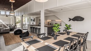 A modern kitchen with white cabinets, a large island, and a hanging fish decoration. - Collie’s beach house (Mangawhai Heads)