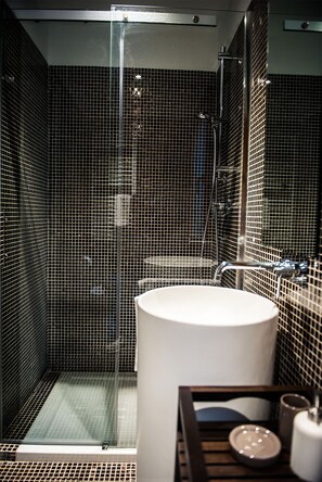 Une salle de bain moderne avec une douche à parois de verre, un lavabo rond et un petit coin coiffeuse.