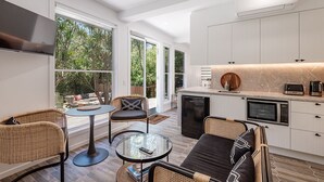 A modern kitchen with white cabinets, a built-in microwave, and a coffee maker. There is a dining area with wicker furniture and a glass table. - "Summer Salt" @ Sunshine + Pets & HEATED POOL 150m to the beach! (Noosa Heads)