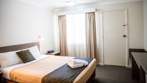 Ein Hotelzimmer mit einem ordentlich bezogenem Bett, einem Nachttisch, einer Lampe und einer Tür.
