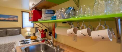 A compact kitchen with a sink, stove, and green shelves holding dishes and mugs.