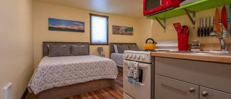 Una habitación pequeña con cama, kitchenette y piso de madera.