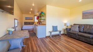 A compact living space with a kitchenette, a dining area, and a seating area with a sofa and a bench. - Cabin 4 · Emigrant Cabins #4- Tiny Cabin for your Adventure (Emigrant)
