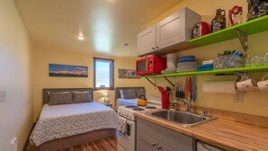 A compact bedroom with a bed, a small kitchenette with a stove and sink, and a window with a view. - Cabin 4 · Emigrant Cabins #4- Tiny Cabin for your Adventure (Emigrant)