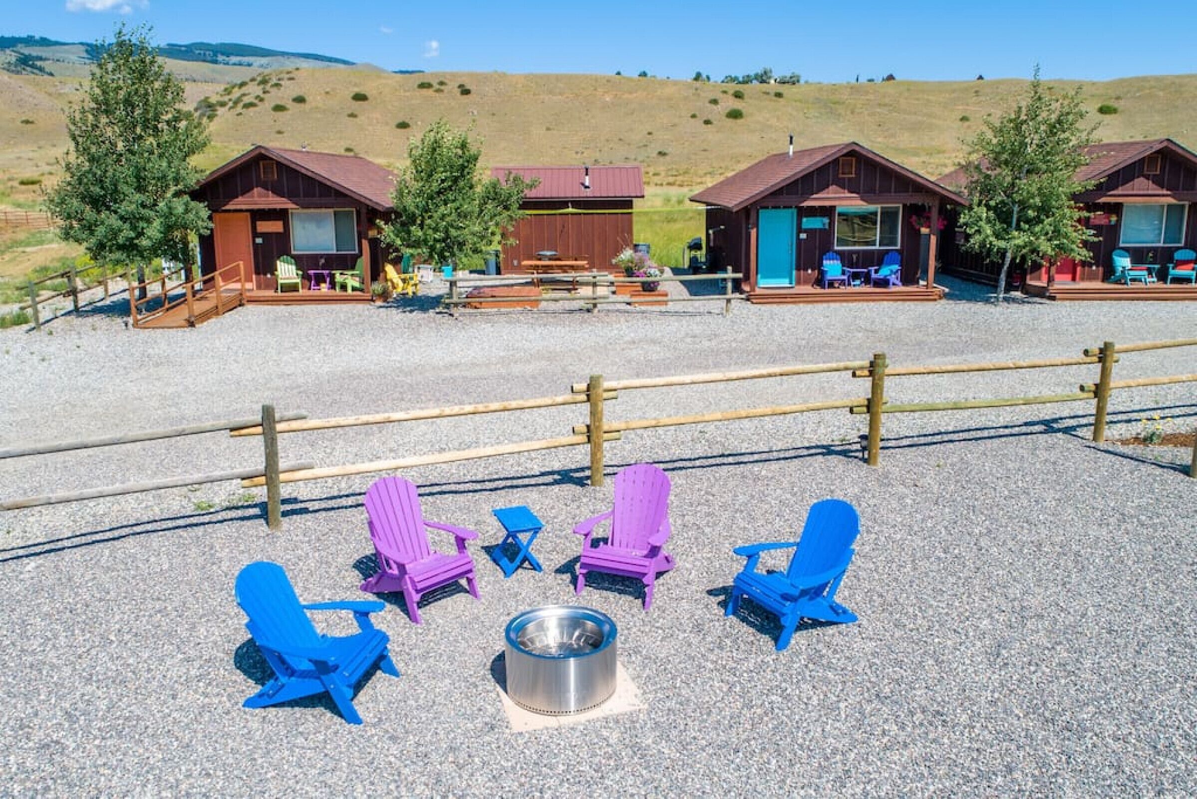 A campground with wooden cabins, outdoor seating, and a gravel area.