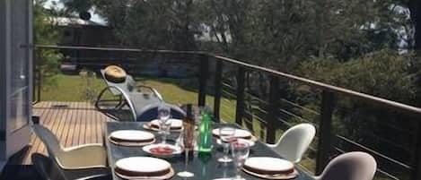 An outdoor dining area with a table set for four, surrounded by chairs, overlooking a forested area.